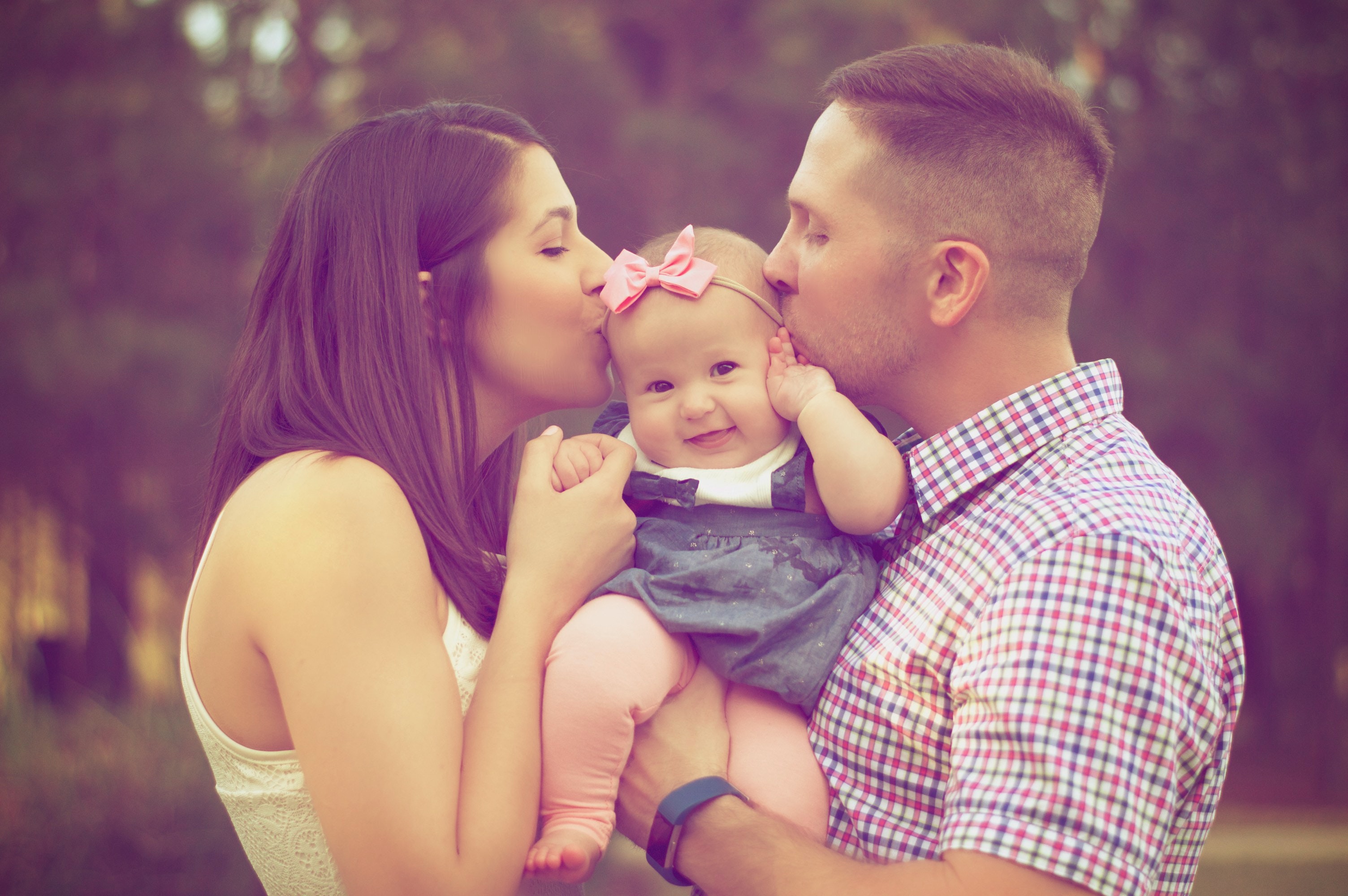 baby girl smiling kissed by man and woman