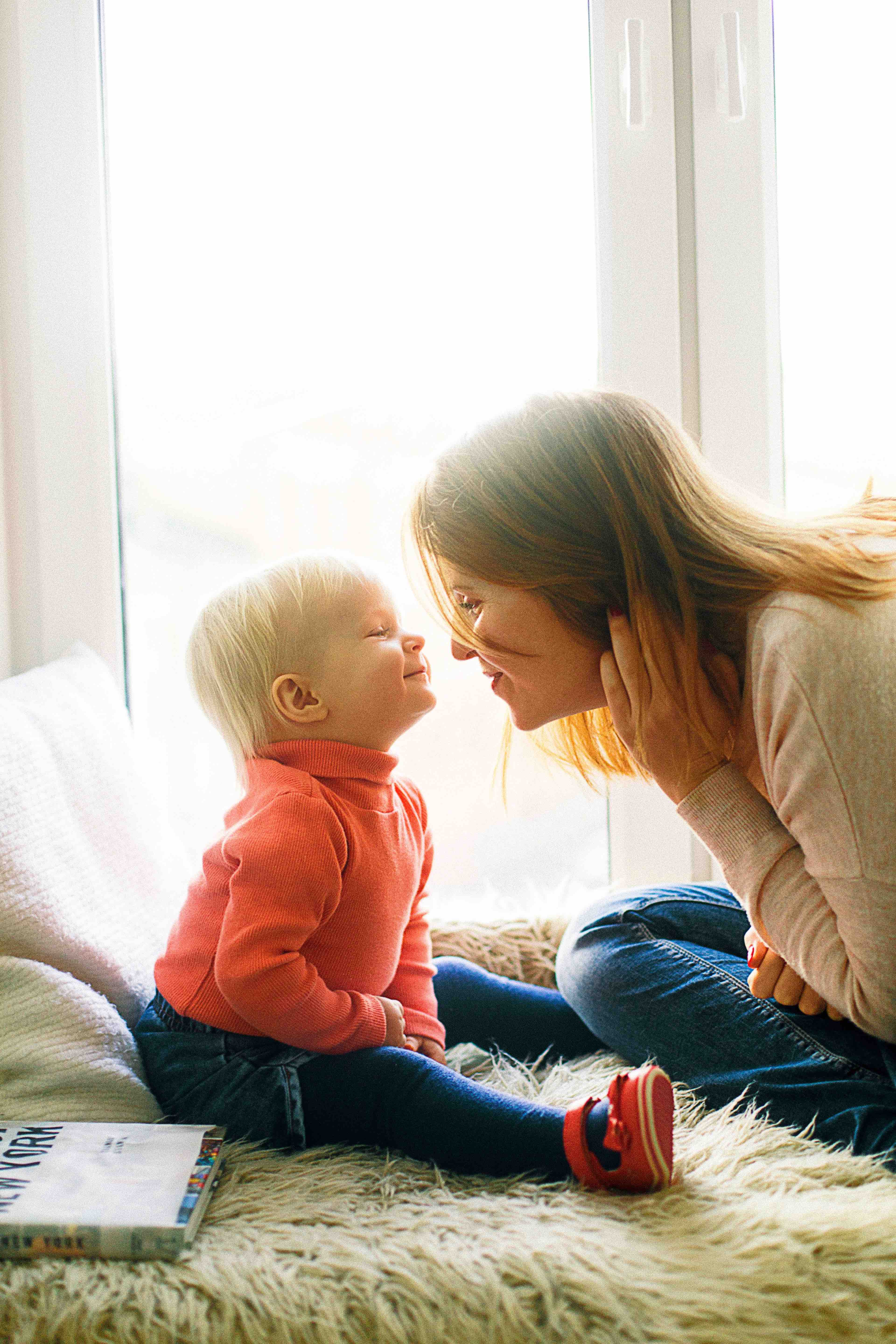 mom with white sweater and baby with orange sweater almost touching noses smiling